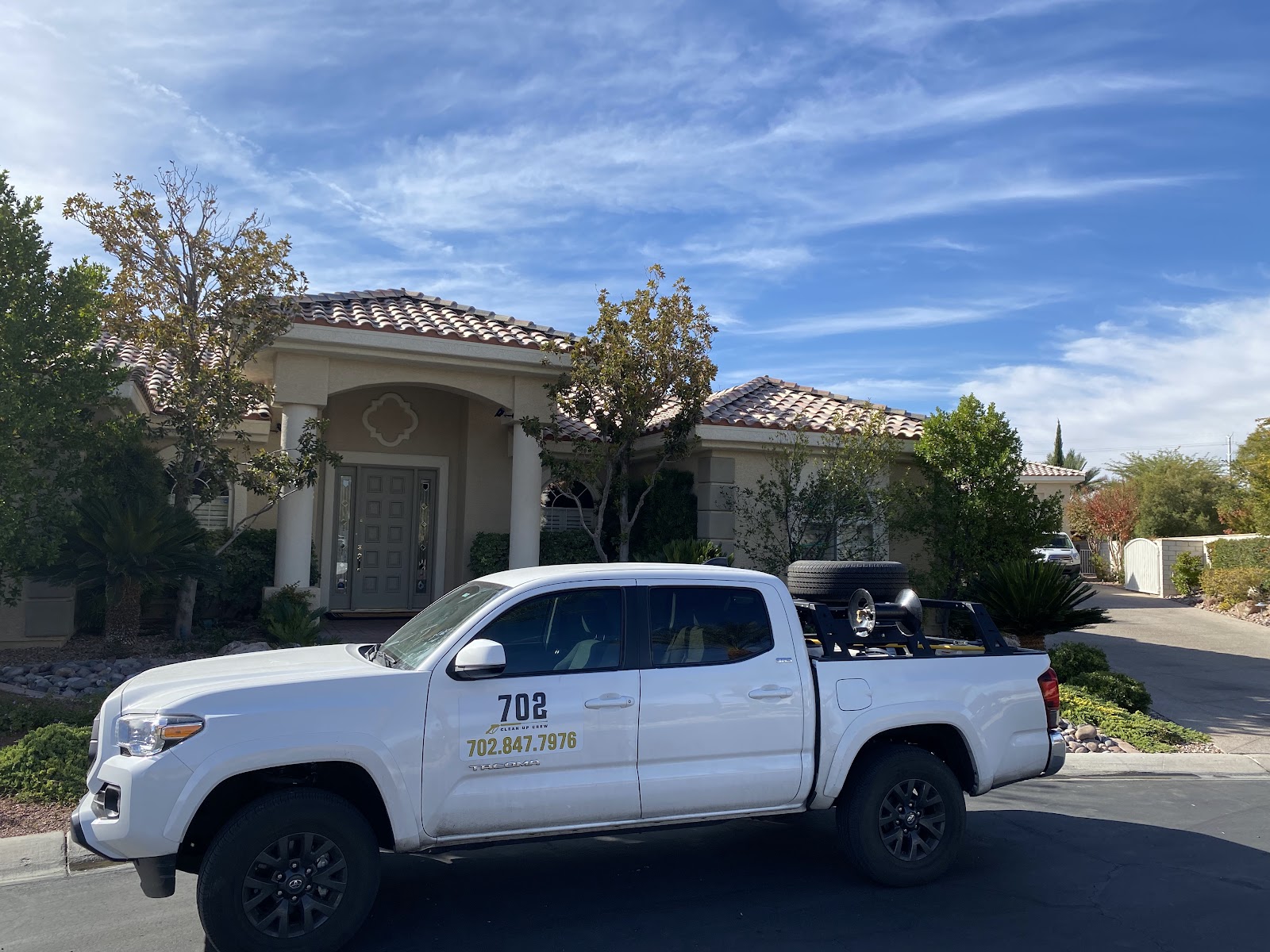 White Toyota Tacoma with 702 branding and equipment parked in front of a home under a blue sky