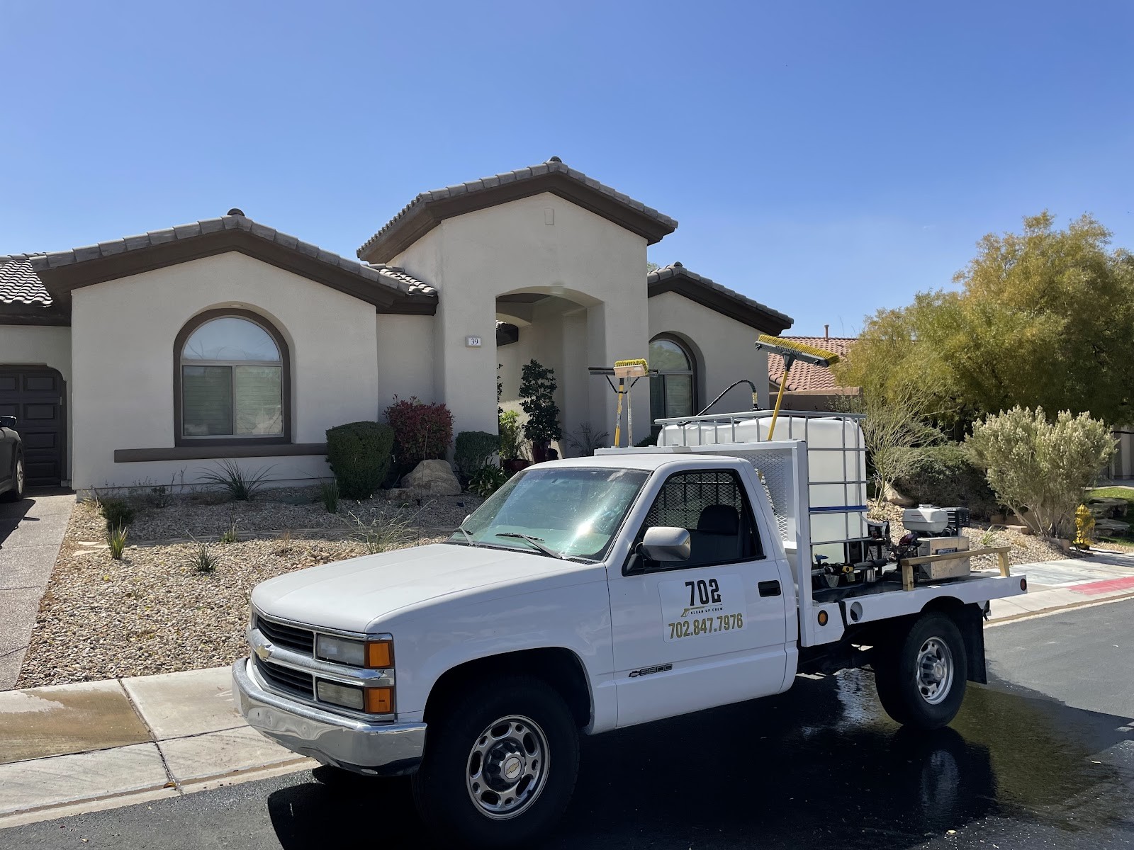 White Chevrolet flatbed work truck with 702 Clean Up Crew branding parked at a home